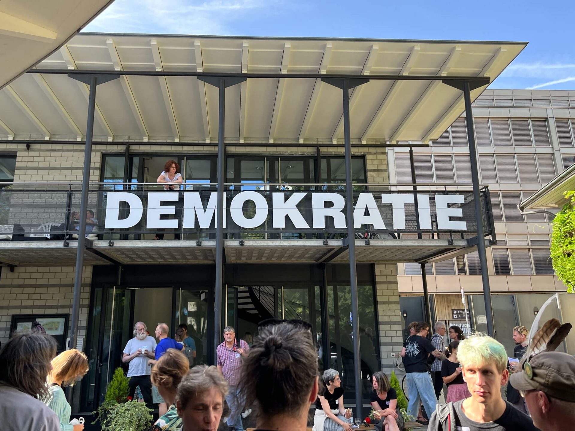 Besucher:innen vor dem Event-Gebäude in Bern. Am Balkon steht in sehr grossen Buchstaben des Wort «Demokratie»